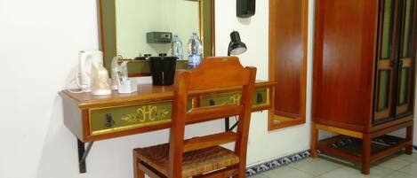 Un escritorio de madera con un espejo, una silla, un teléfono y un mueble bajo.