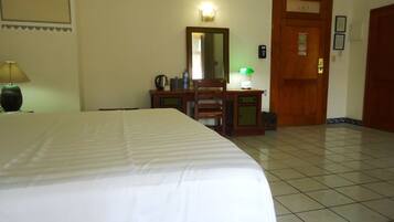 A hotel room with a bed, a desk with a chair, a mirror, a lamp, and a door.