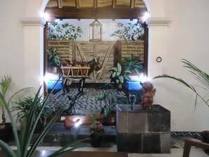 A decorative fountain with a donkey, a cart, and a bear statue in a tiled area with plants.