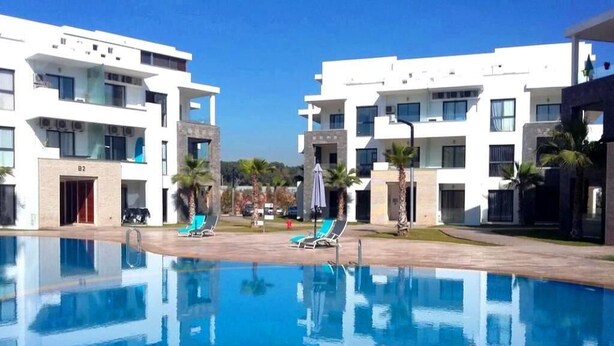 Ett modernt hotell med en swimmingpool, flera balkonger och palmer.