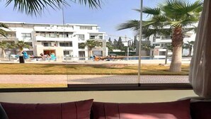 Ett rum med utsikt över ett poolområde, palmer och en modern byggnad i bakgrunden.