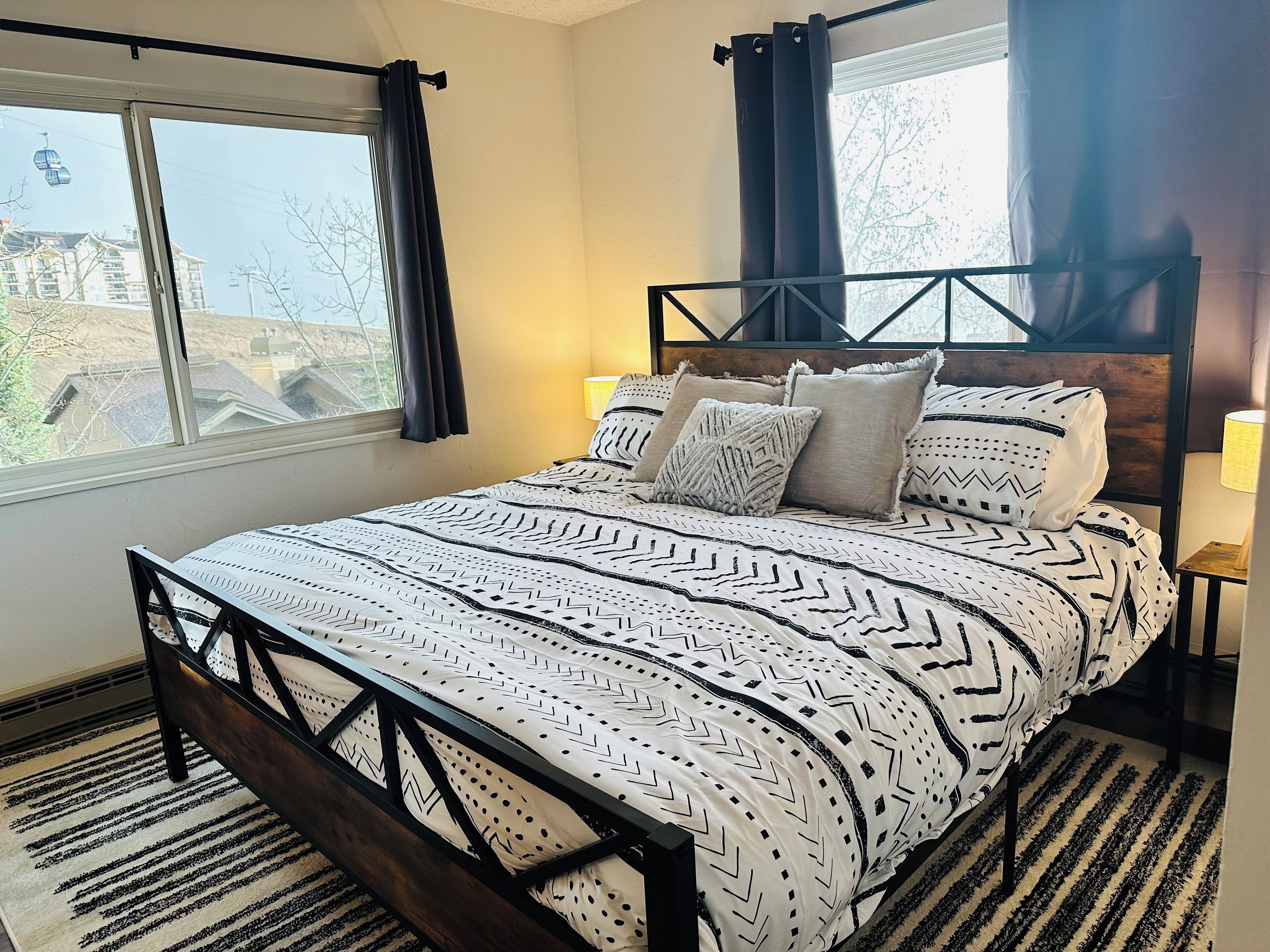 A bedroom with a bed, a window, and a view of buildings outside.