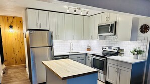 Une cuisine moderne avec des armoires blanches, des appareils en acier inoxydable et un îlot central en bois.