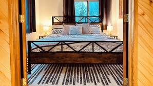 Une chambre à coucher avec un lit en bois, une literie à motifs et une vue sur les arbres par la fenêtre.