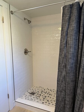 A shower with white tiled walls, a metal showerhead, and a shower curtain. - Mountainside Condo: King Bed/Hot Tub/On Free Bus Route/Fireplace (Steamboat Springs)