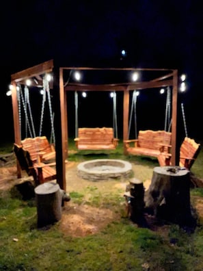 A wooden gazebo with four benches and a central fire pit, surrounded by trees. - 5-bedroom lodge near Ozark National Forest and Lake Fort Smith state park. (Mountainburg)