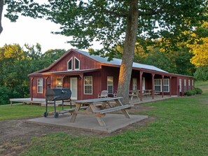 Relax on the porch with a bench and picnic table, surrounded by a well-maintained lawn and a large tree.