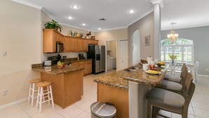 A modern kitchen with granite countertops, wooden cabinets, stainless steel appliances, and a central island with stools. - Private Heated Pool & Beach House: 3 King Beds , TVs throughout, 1000mbps WiFi (Vero Beach)
