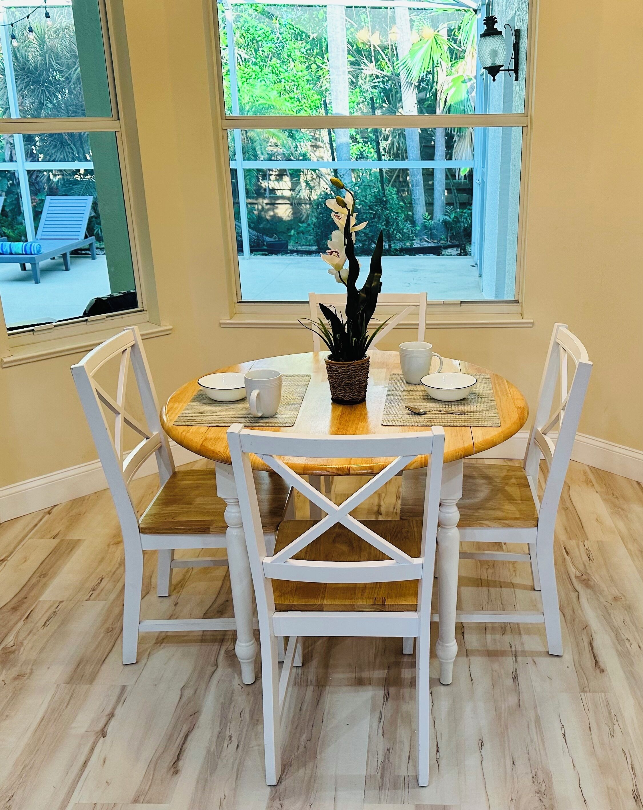 A dining area with a round wooden table, white chairs, and a potted plant.