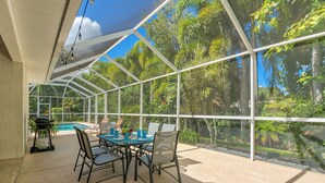 A covered outdoor dining area with a view of a swimming pool and tropical vegetation. - Private Heated Pool & Beach House: 3 King Beds , TVs throughout, 1000mbps WiFi (Vero Beach)