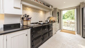 A kitchen with a black stove, white cabinets, and a view of the outdoors through a glass door. - Manor Farmhouse, Cruxton, Dorchester (Cruxton)