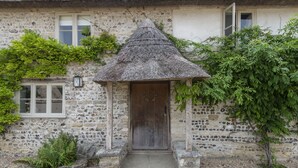 A stone house with a thatched-roof entrance, a wooden door, and a small porch. - Manor Farmhouse, Cruxton, Dorchester (Cruxton)