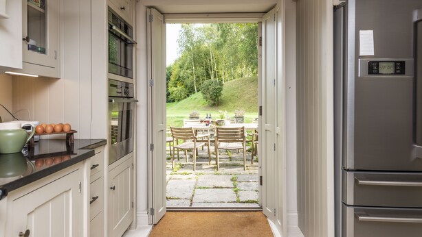 A kitchen with white cabinets, a stainless steel refrigerator, and a view of a patio with a table and chairs. - Manor Farmhouse, Cruxton, Dorchester (Cruxton)