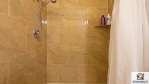 A bathroom with a shower, tiled walls, and a shelf with toiletries.