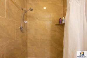 Un baño con ducha, paredes de azulejos y un estante con artículos de aseo.