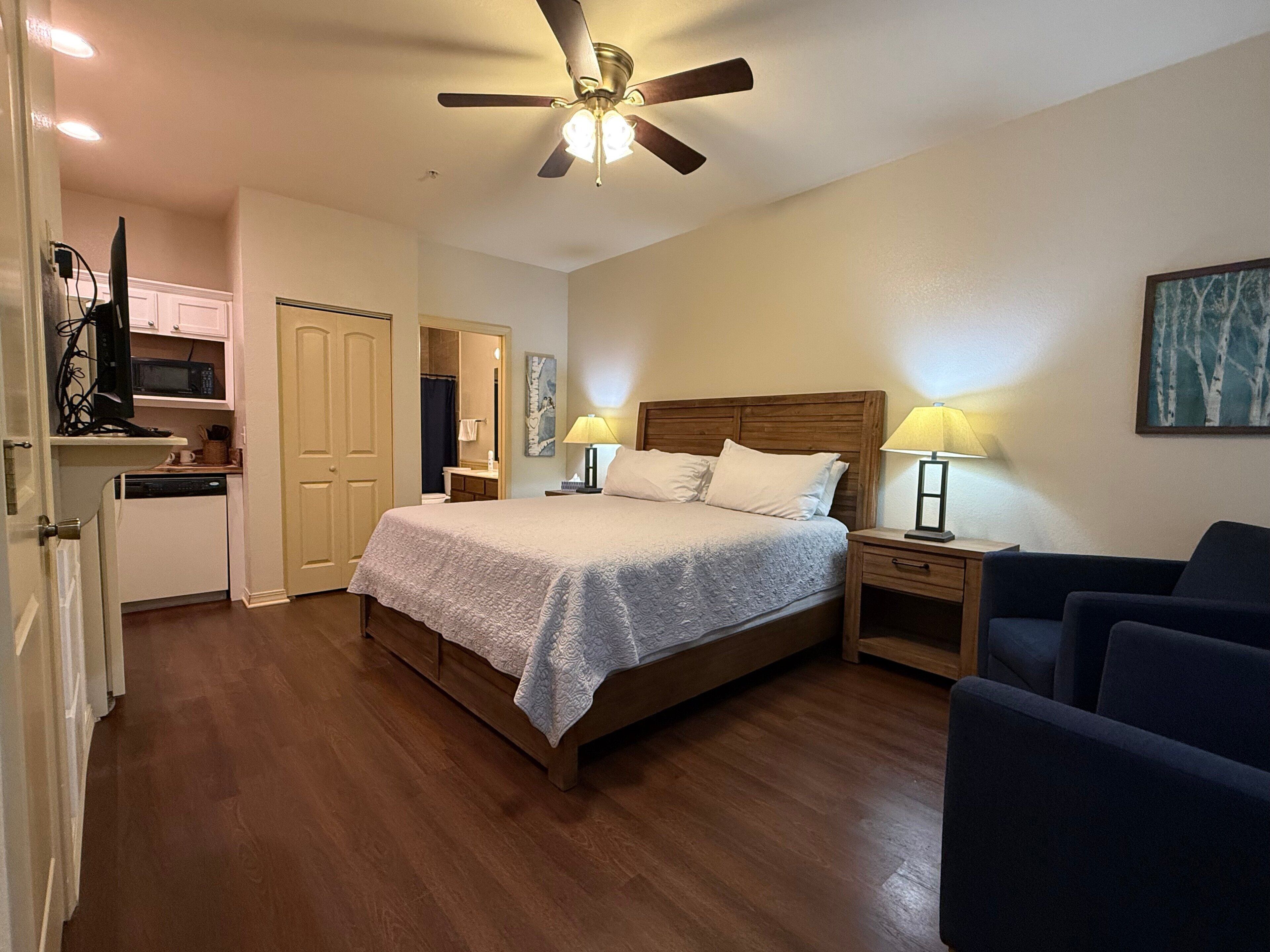 Une chambre à coucher avec un lit, des lampes de chevet, un ventilateur de plafond, une tête de lit en bois et une petite table de chevet.