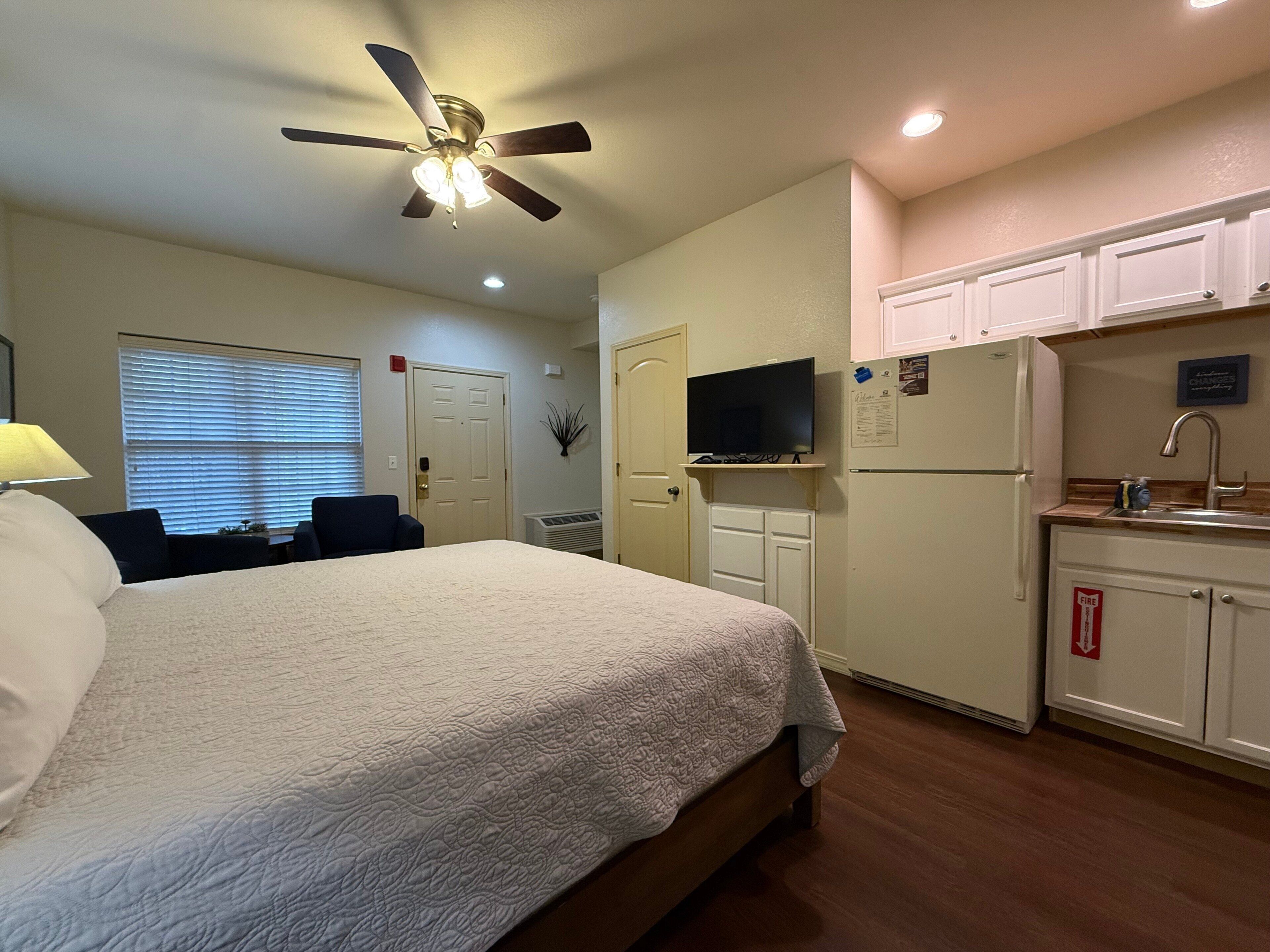 Une chambre d’hôtel équipée d’un lit, d’un ventilateur de plafond, d’une télévision, d’un réfrigérateur et d’un petit coin cuisine.
