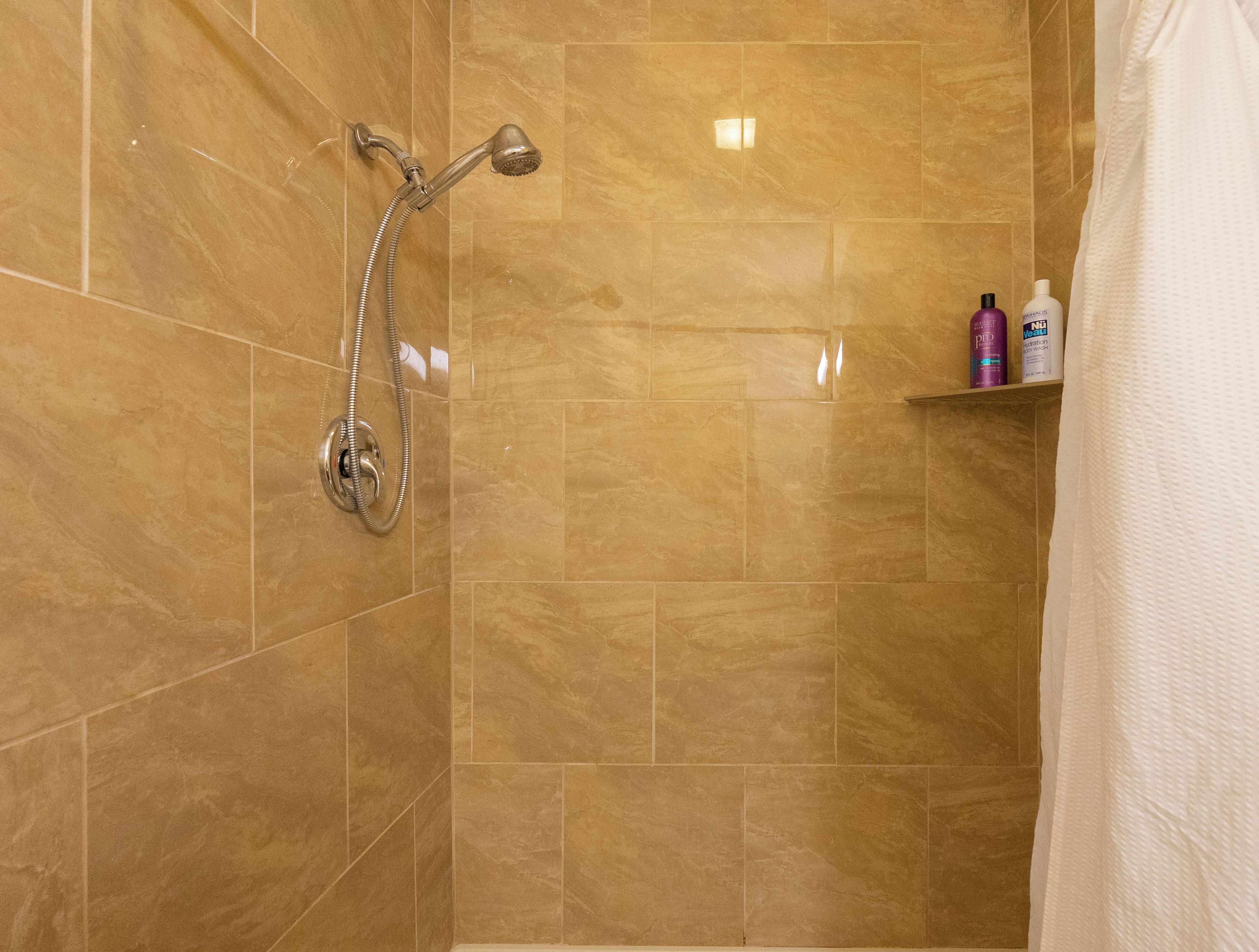 Une salle de bain avec une douche, des murs carrelés et une étagère contenant des articles de toilette.
