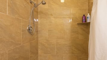 Une salle de bain avec une douche, des murs carrelés et une étagère contenant des articles de toilette.