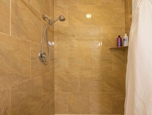 A bathroom with a shower, tiled walls, and a shelf with toiletries.