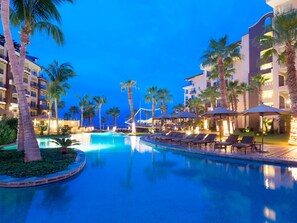 A resort pool area with palm trees, lounge chairs, and a clear blue sky at dusk.