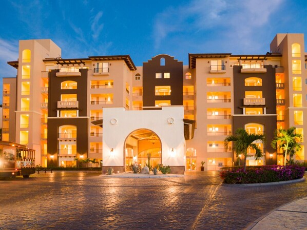 A hotel with a central archway entrance, multiple balconies, and a courtyard with palm trees.