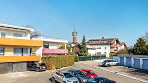 A parking lot with several cars, buildings with balconies, and a tower with a spire. - Cosy Studio Apartment in Quiet Area with Wi-Fi, Terrace & Garden (Pforzheim)