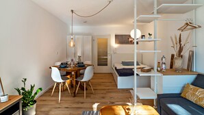 A modern, compact living space with a dining area, a sofa, a hanging light fixture, and a small bookshelf. - Cosy Studio Apartment in Quiet Area with Wi-Fi, Terrace & Garden (Pforzheim)