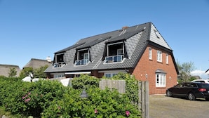 A two-story house with a sloped roof, a visible attic, and a car parked in the driveway. - Heefwai Wohnung 6 (Sylt)