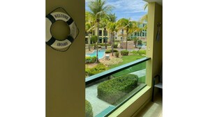A view from a hotel room with a balcony overlooking a pool area, palm trees, and a building with a 'WELCOME' sign. - Enjoy Paradise-"AQUATIKA" Beach Front-5 POOLS!! UNIT WITH WATER RESERVE SYSTEM!! (Loiza)