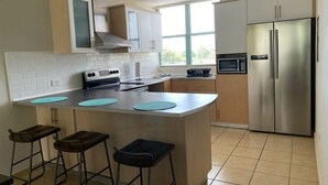 A kitchen with a central island, bar stools, a stainless steel refrigerator, a microwave, and a stove. - Enjoy Paradise-"AQUATIKA" Beach Front-5 POOLS!! UNIT WITH WATER RESERVE SYSTEM!! (Loiza)