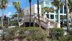 A hotel with a central staircase, palm trees, and a well-maintained garden. - Enjoy Paradise-"AQUATIKA" Beach Front-5 POOLS!! UNIT WITH WATER RESERVE SYSTEM!! (Loiza)