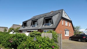 A two-story house with a sloped roof, a visible attic, and a car parked in the driveway. - Heefwai Wohnung 2 (Sylt)