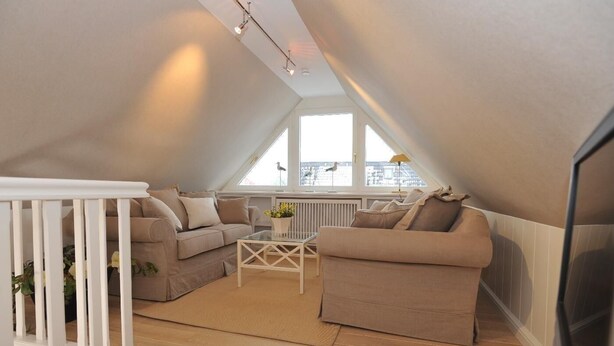 A modern loft apartment with a high ceiling, two beige sofas, a glass coffee table, and a white railing. - Biberhüs OG (Sylt)