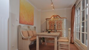 A dining area with a wooden table and chairs, a bench with checkered cushions, and a decorative cabinet with floral patterns. - Biberhüs OG (Sylt)