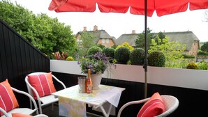 A patio with wicker chairs and a table, a red umbrella, and a potted plant. - Biberhüs OG (Sylt)