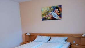 Een slaapkamer met een houten bed, nachtkastje, bijzettafeltje en een schilderij aan de muur.