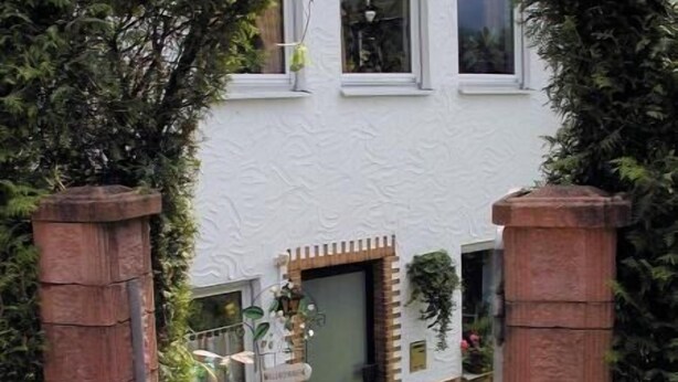 Een huis met een witte gevel, een bakstenen entree en een tuin met een klein vijvertje en planten.