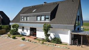 A two-story house with a sloped roof, a front porch, and a garage. - Feskerdam 28 OG (Sylt)