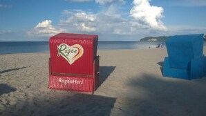 Une chaise de plage rouge, ornée d’un logo en forme de cœur et portant le nom « Rügen », sur une plage de sable.