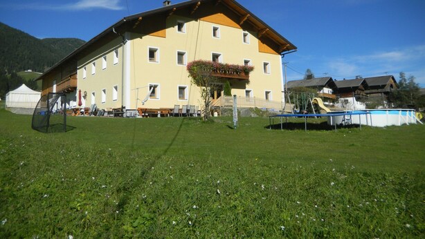 A large building with multiple windows and a balcony with flowers. - Ferienwohnung Dolomitenblick (Strassen)