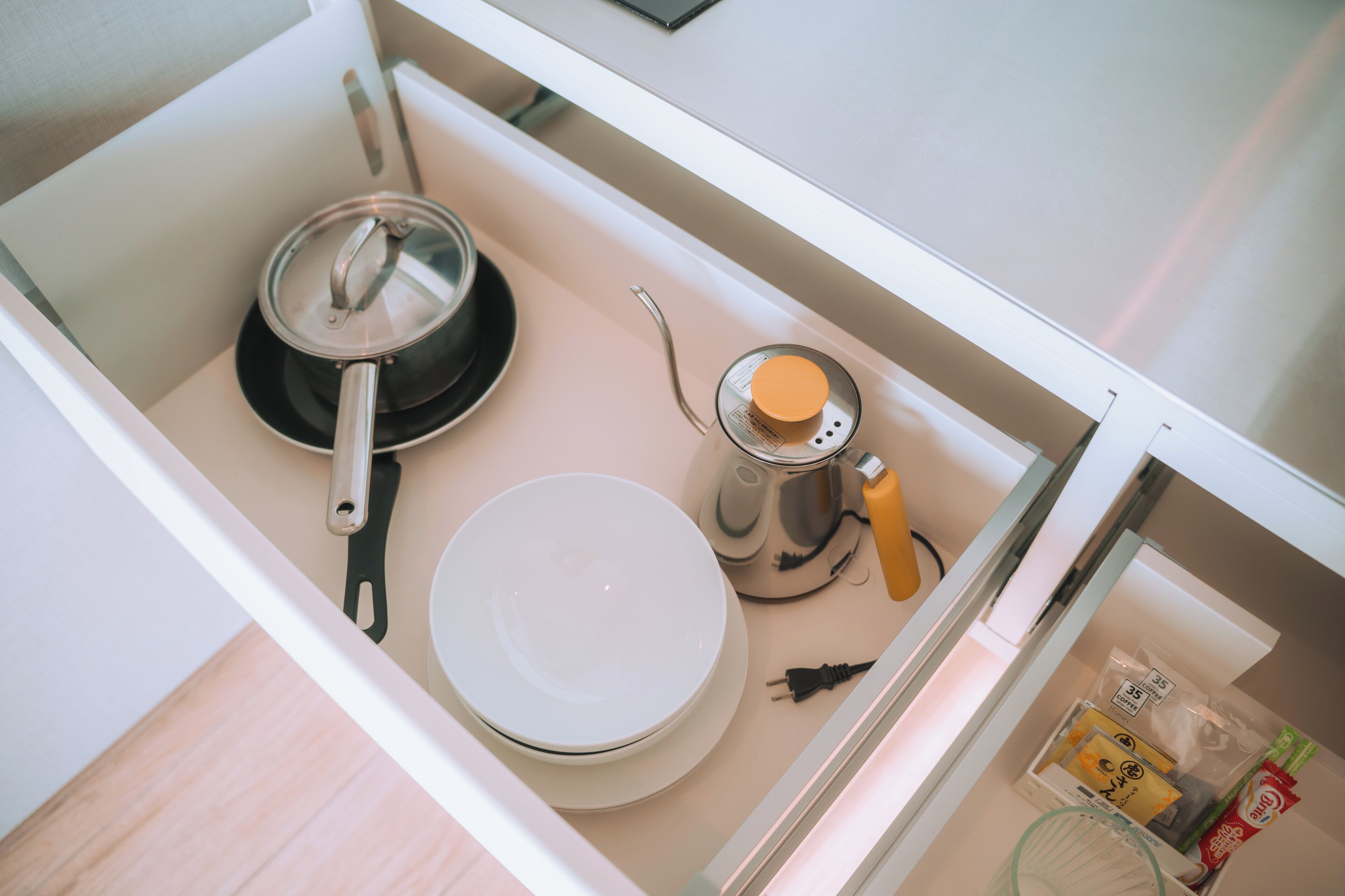 A kitchen with a stove, a kettle, a bowl, and a coffee maker.