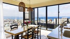 Een moderne keuken met een groot raam, een eethoek met tafel en stoelen, en uitzicht op de stad en zee.