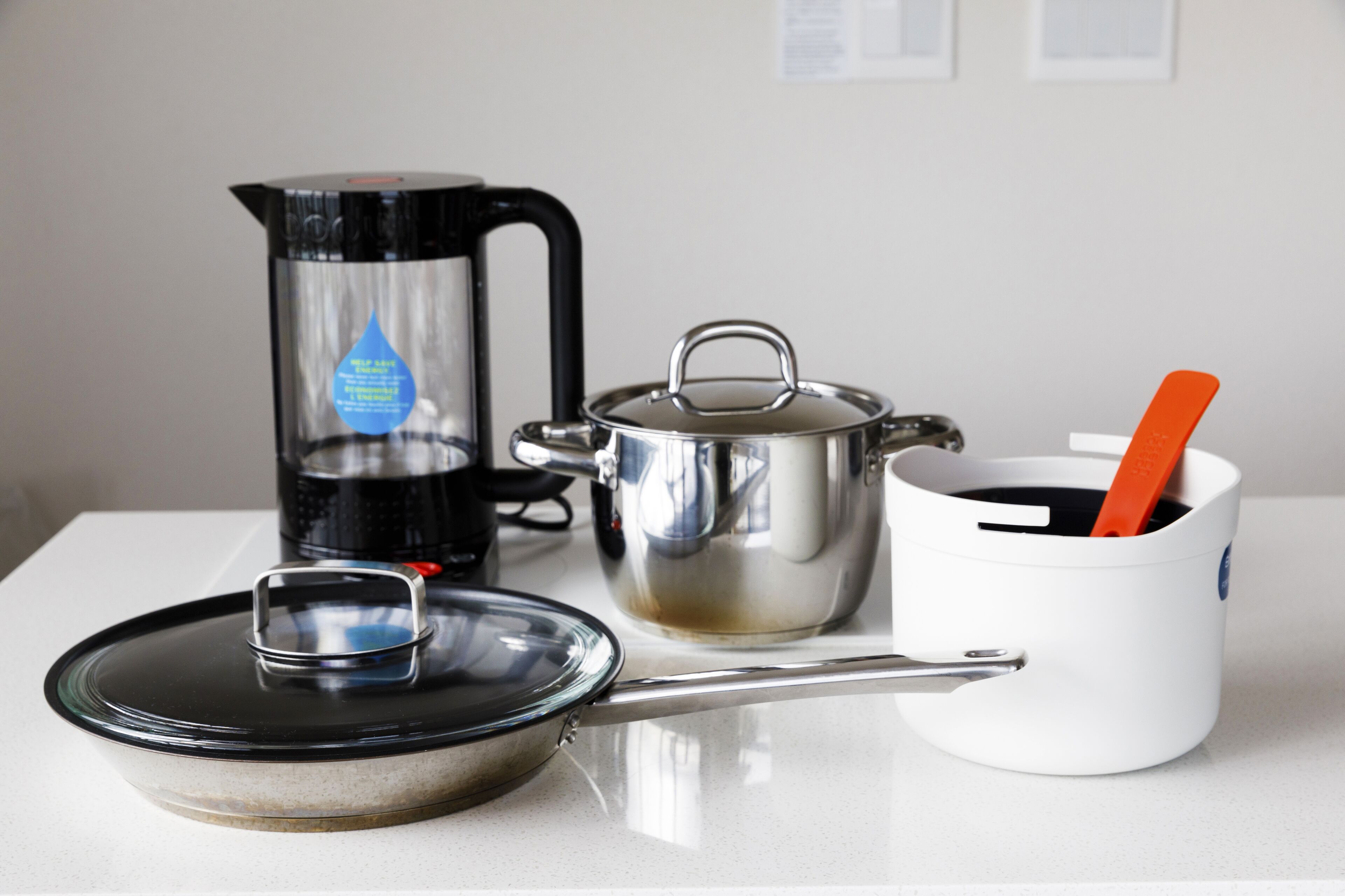 Eine Küchenarbeitsplatte mit Kaffeemaschine, Topf, Pfanne und einer weißen Tasse mit Löffel.