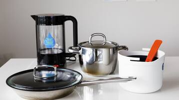 Eine Küchenarbeitsplatte mit Kaffeemaschine, Topf, Pfanne und einer weißen Tasse mit Löffel.