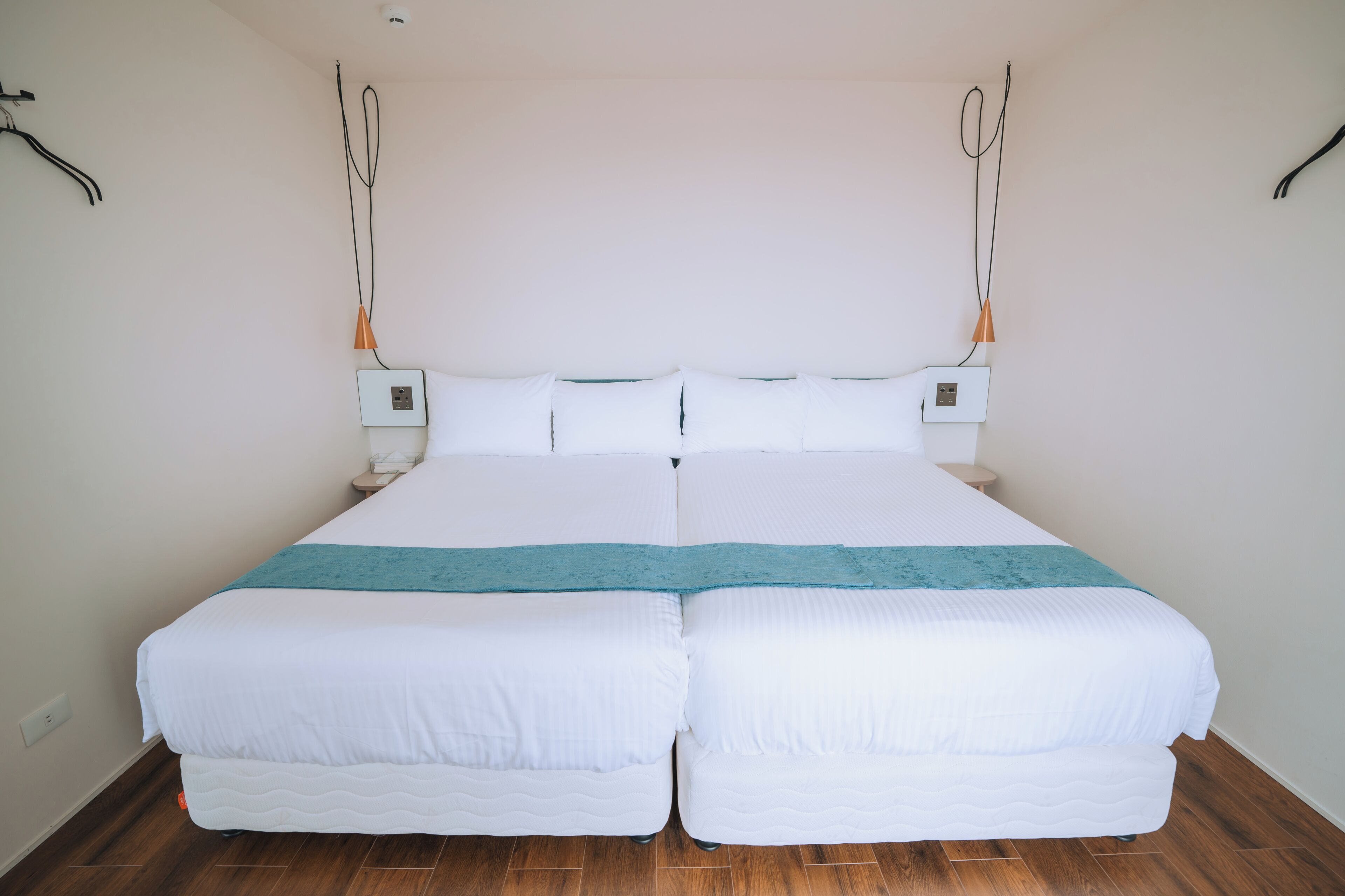 A double bed with white bedding and a teal accent, two bedside tables, and a wooden floor.