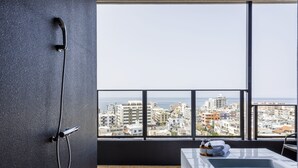 Une salle de bain moderne dotée d’une baignoire, d’une douche et offrant une vue sur le paysage urbain grâce à de grandes fenêtres.