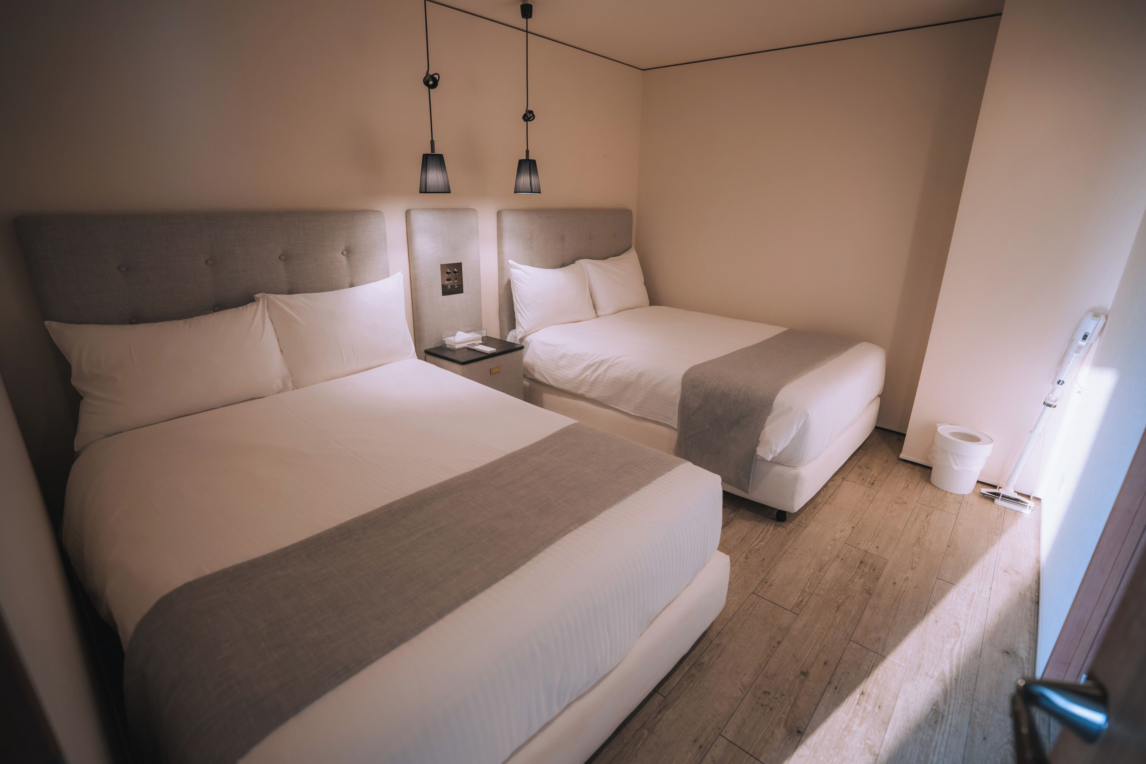 A hotel room with two beds, a nightstand, a lamp, and a wooden floor.