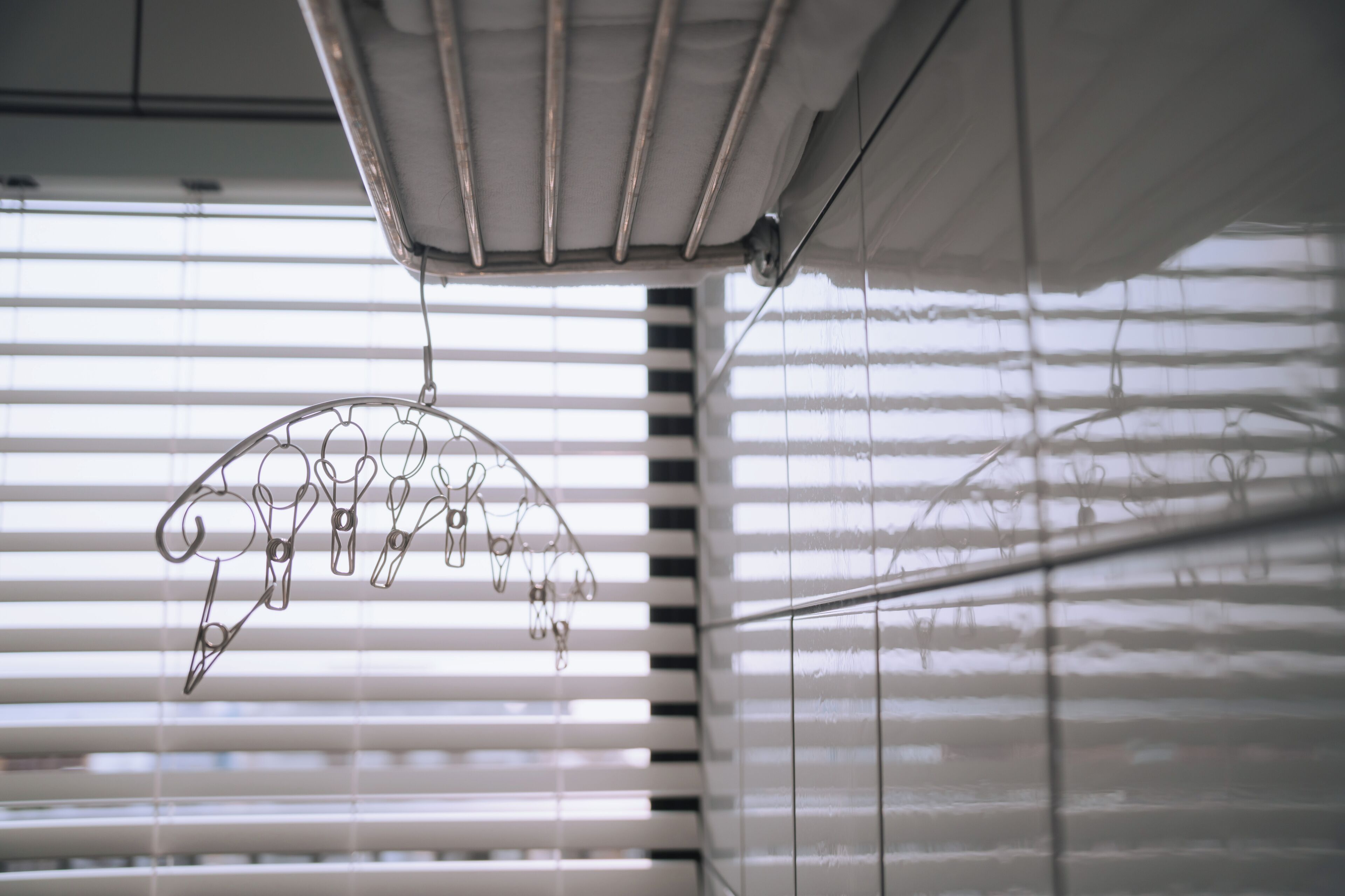 A ceiling with a metal rack and a hanging object, blinds on the window, and a wall with a grid pattern.