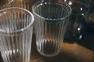 Primer plano de vasos de vidrio transparente con textura acanalada, sobre una superficie de madera.